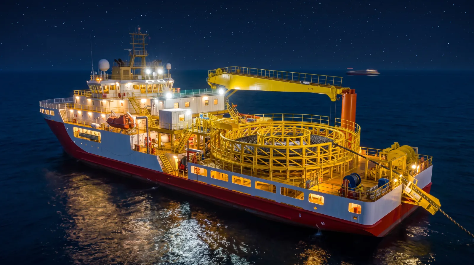 A cable-lay vessel working offshore at night, deck fully illuminated